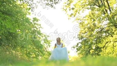 快乐浪漫时尚的金发新娘穿着白色连衣裙，在阳光下在森林里奔跑和旋转